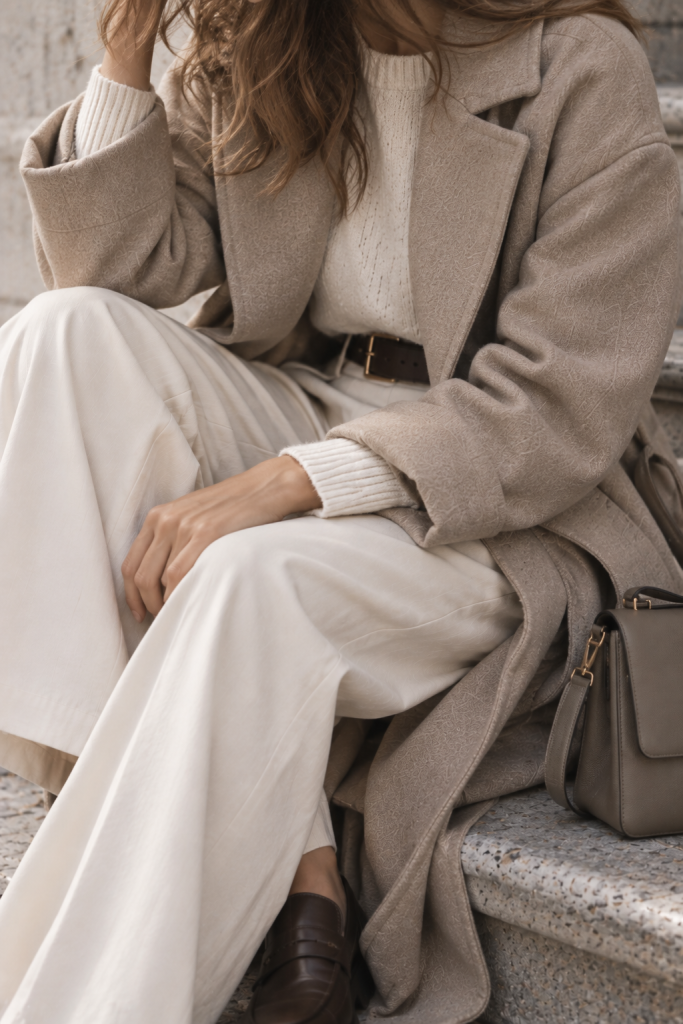 Layering mit taupefarbenem Mantel, hellem Strickpullover und cremefarbener Stoffhose für Herbst und Winter