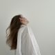 Frau im weißen Oversize-Hemd mit offenem Haar vor heller, minimalistischer Wand – moderner Ausdruck der lässigen Eleganz der Parisienne.