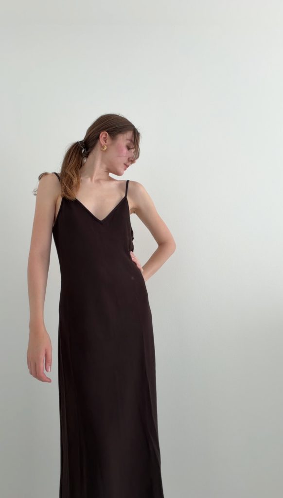 Outfit Proportionen am Beispiel eines dunkelbraunen Maxikleids mit schmalen Trägern und fließendem Schnitt vor hellem Hintergrund.