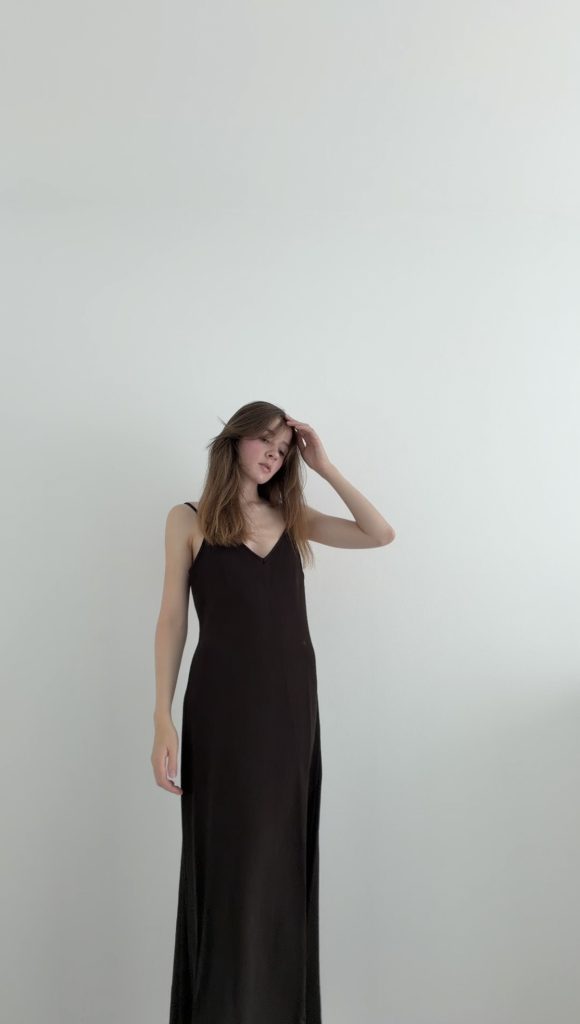 Outfit Proportionen in einer minimalistischen Ganzkörperaufnahme mit langem dunkelbraunem Trägerkleid vor weißem Hintergrund.
